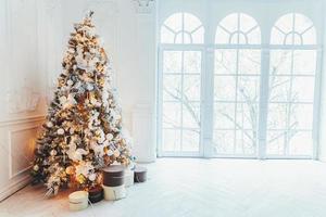 Classic christmas New Year decorated interior room New year tree. Christmas tree with gold decorations. Modern white classical style interior design apartment, large window. Christmas eve at home. photo