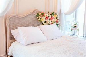 hermoso y lujoso dormitorio interior clásico, blanco, brillante y limpio, de estilo barroco, con cama king-size, ventana grande, sillón y composición floral. foto