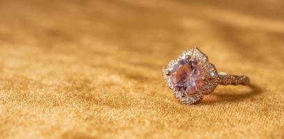 Jewelry pink diamond ring on golden fabric background close up photo