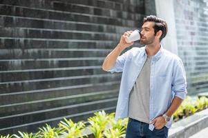 Young caucasian man drinking coffee and wearing casual shirt while walking on his way for relax on his holiday. photo