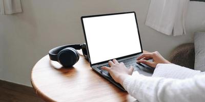 Girl typing on laptop with blank screen,  headphones on wooden table, mock up photo