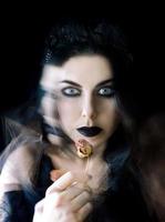 mujer gótica de cabello oscuro con labios negros maquillados y rosa seca en la mano foto
