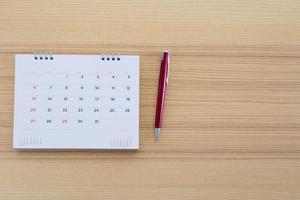 página de calendario con bolígrafo sobre fondo de mesa de madera foto