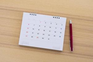 página de calendario con bolígrafo sobre fondo de mesa de madera foto