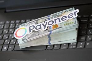 TERNOPIL, UKRAINE - SEPTEMBER 6, 2022 Payoneer paper logotype lies on black laptop with US dollar bills. Payoneer is American financial services company that provides online money transfer photo