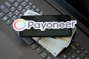 TERNOPIL, UKRAINE - SEPTEMBER 6, 2022 Payoneer paper logotype lies on black laptop with US dollar bills. Payoneer is American financial services company that provides online money transfer photo