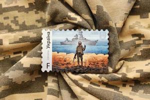 TERNOPIL, UKRAINE - SEPTEMBER 2, 2022 Famous Ukrainian postmark with russian warship and ukrainian soldier as wooden souvenir on army camouflage uniform photo
