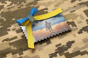 TERNOPIL, UKRAINE - SEPTEMBER 2, 2022 Famous Ukrainian postmark with russian warship and ukrainian soldier as wooden souvenir on army camouflage uniform photo