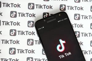 TERNOPIL, UKRAINE - MAY 2, 2022 Tik Tok smartphone app on screen and Many TikTok logo printed on paper. Tiktok or Douyin is a famous Chinese short-form video hosting service owned by ByteDance photo