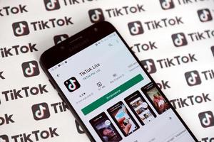 TERNOPIL, UKRAINE - MAY 2, 2022 Tik Tok smartphone app on screen and Many TikTok logo printed on paper. Tiktok or Douyin is a famous Chinese short-form video hosting service owned by ByteDance photo