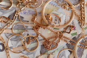 muchos costosos anillos, aretes y collares de joyería de oro con una gran cantidad de billetes de dinero ucraniano. concepto de tienda de empeño o joyería. comercio de joyas foto