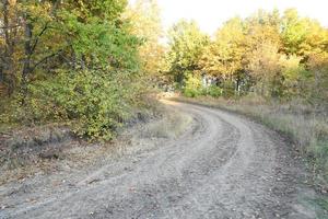 Autumn landscape with a curved road and traces of the tread of large wheels of agricultural machinery photo