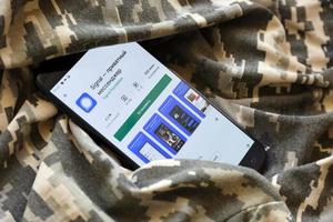 TERNOPIL, UKRAINE - APRIL 24, 2022 Signal Private Messenger app play store page on the display of a black mobile smartphone on ukrainian military camouflage photo