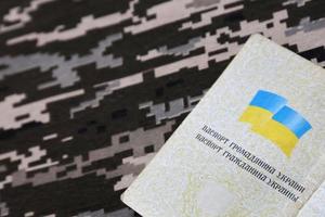 Ukrainian foreign passport on fabric with texture of military pixeled camouflage. Cloth with camo pattern in grey, brown and green pixel shapes and Ukrainian ID photo