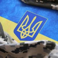 Ukrainian flag and coat of arms with fabric with texture of pixeled camouflage. Cloth with camo pattern in grey, brown and green pixel shapes with Ukrainian trident sign photo