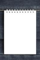 White notebook with clean pages lying on dark blue jeans background. Image with copy space photo