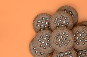 Detailed picture of dark brown round sandwich cookies with coconut filling on an orange surface. Background image of a close-up of several treats for tea photo