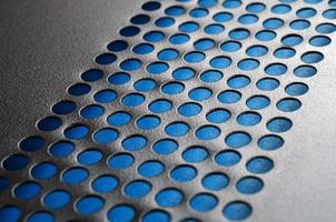 Black metal computer case panel mesh with holes on blue background. Abstract close up image photo