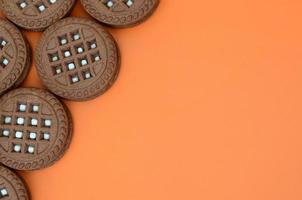 Detailed picture of dark brown round sandwich cookies with coconut filling on an orange surface. Background image of a close-up of several treats for tea photo