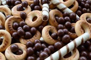 A lot of crispy sweet tubules, chocolate melting balls and yellow bagels lie on a wooden surface. Close up view photo