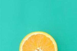 Top view of a one orange fruit slice on bright background in turquoise green color. A saturated citrus texture image photo