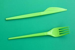 cubiertos desechables de plastico verde. tenedor y cuchillo de plástico yacen sobre una superficie de fondo verde foto