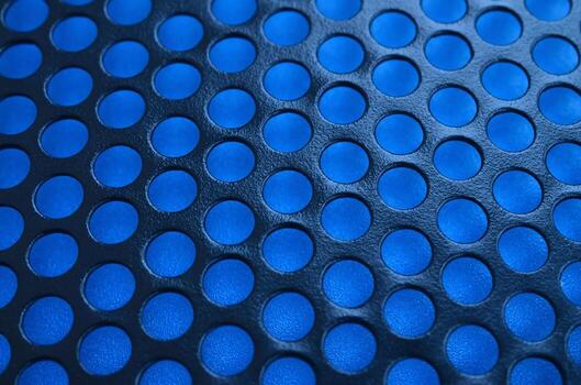 Black metal computer case panel mesh with holes on blue background. Abstract close up image photo