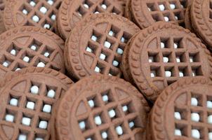 Detailed picture of dark brown round sandwich cookies with coconut filling close up. Background image of several treats for tea photo