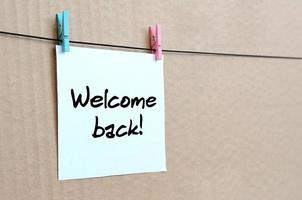 Welcome back Note is written on a white sticker that hangs with a clothespin on a rope on a background of brown cardboard photo