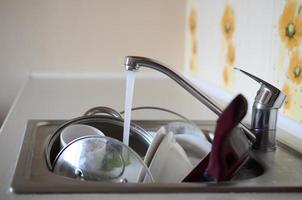 Dirty dishes and unwashed kitchen appliances lie in foam water under a tap from a kitchen faucet photo