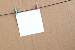 White blank card on rope on a brown cardboard background. Creative reminder, small sheet of paper on wooden clothespin, memo backdrop photo