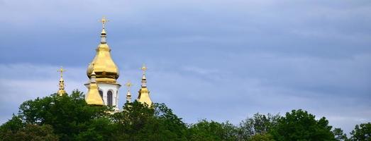 cúpulas doradas de una iglesia ortodoxa entre árboles florecientes sobre un fondo de cielo azul nublado foto