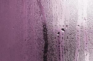 textura de una gota de lluvia sobre un fondo transparente húmedo de vidrio. tonificado en color rosa