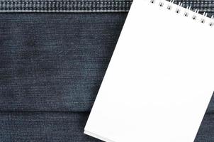 White notebook with clean pages lying on dark blue jeans background. Image with copy space photo