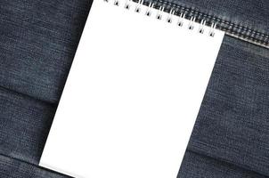 White notebook with clean pages lying on dark blue jeans background. Image with copy space photo