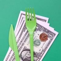 Disposable plastic cutlery green. Plastic fork and knife lie on a small amount of US dollars photo