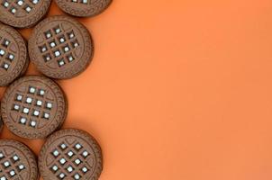 Detailed picture of dark brown round sandwich cookies with coconut filling on an orange surface. Background image of a close-up of several treats for tea photo