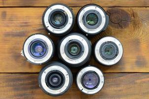 Several photographic lenses lie on a brown wooden background. Space for text photo