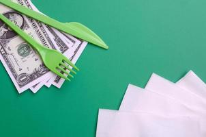 Disposable plastic cutlery green. Plastic fork and knife lie on a small amount of US dollars next to napkins photo