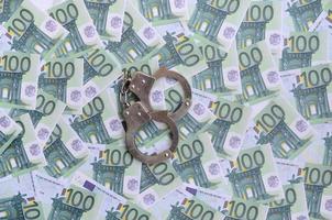 Police handcuffs lies on a set of green monetary denominations of 100 euros. A lot of money forms an infinite heap photo