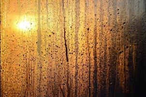 The texture of misted glass with a lot of drops and drips of condensation against the sunlight at dawn. Background image photo