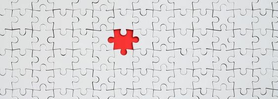 The texture of a white jigsaw puzzle in an assembled state with one missing element forming a red space photo