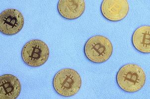 Many golden bitcoins lies on a blanket made of soft and fluffy light blue fleece fabric. Physical visualization of virtual crypto currency photo