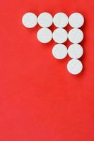 Several white tablets lie on a bright red background in the form of a triangular arrow. Background image on medicine and pharmaceutical topics photo