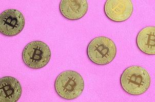 muchos bitcoins dorados se encuentran sobre una manta hecha de suave y esponjosa tela de lana rosa claro. visualización física de moneda criptográfica virtual foto