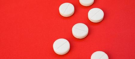 A few white tablets lie on a bright red background surface. Background image on medical and pharmaceutical topics photo