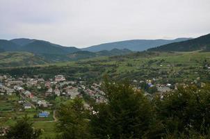 A beautiful view of the village of Mezhgorye, Carpathian region. A lot of residential buildings surrounded by high forest mountains and long river photo