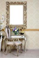 A fragment of a retro interior with a chair and table, on which is a telephone and a vase of flowers. Above the table hangs an empty picture frame for your photo
