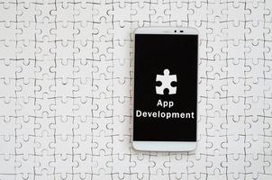 A modern big smartphone with a touch screen lies on a white jigsaw puzzle in an assembled state with inscription. App development photo
