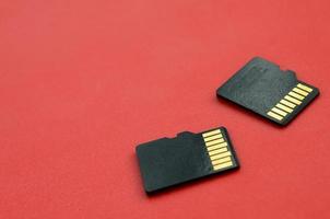 dos pequeñas tarjetas de memoria micro sd se encuentran sobre un fondo rojo. un pequeño y compacto almacén de datos e información foto